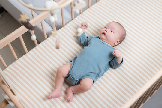 Baby lying inside a wooden crib under a toy