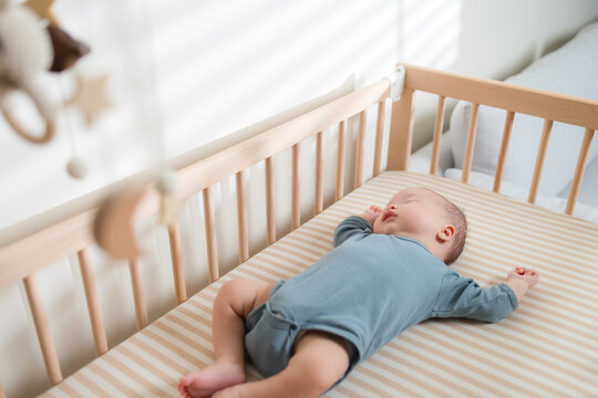 Baby resting peacefully in a wooden crib on a striped sheet