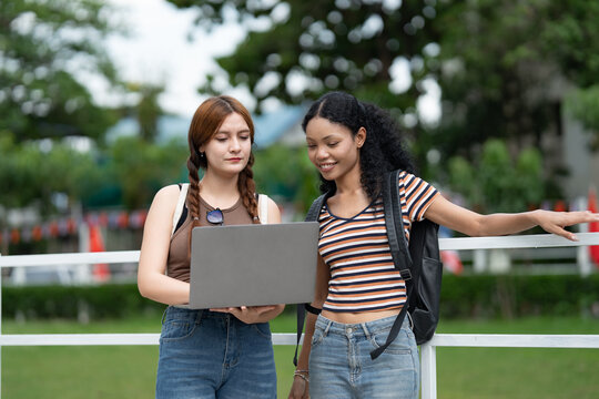 Asia and African American woman student college talking with notebook computer outdoor
