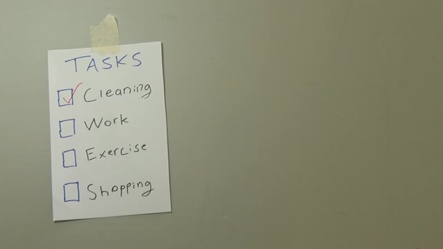 Close-up of a hand checking off completed tasks on a wall-mounted to-do list, illustrating daily planning, productivity, organization, and everyday task management.