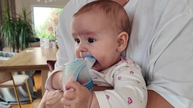Adorable 6-7 month old infant looking at camera while breathing through nebulizer inhaler. Pediatric home care and respiratory illness therapy