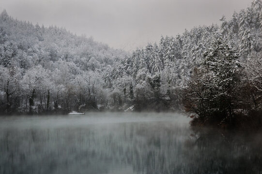View of Lago di Boccafornace surrounded by snow-covered trees and rising mist in winter in Valfornace, Marche, Italy.