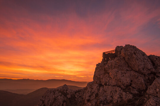 View of Rocca Calascio at sunset with vibrant orange and red sky over the rugged mountainous landscape of Calascio, Abruzzo, Italy.