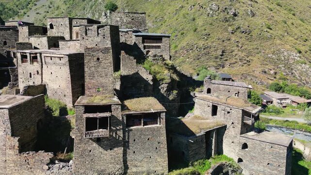 Close aerial drone footage of Shatili fortress village showing stone walls, wooden balconies, flat roofs with vegetation and details of the historic buildings.