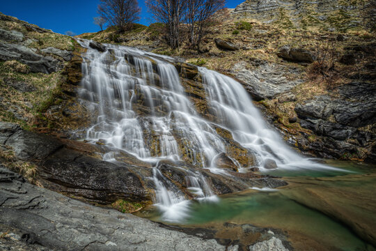 View of the Cento Fonti di Cesacastina waterfall cascading over rocky terrain into a clear pool in the mountains of Crognaleto, Abruzzo, Italy.