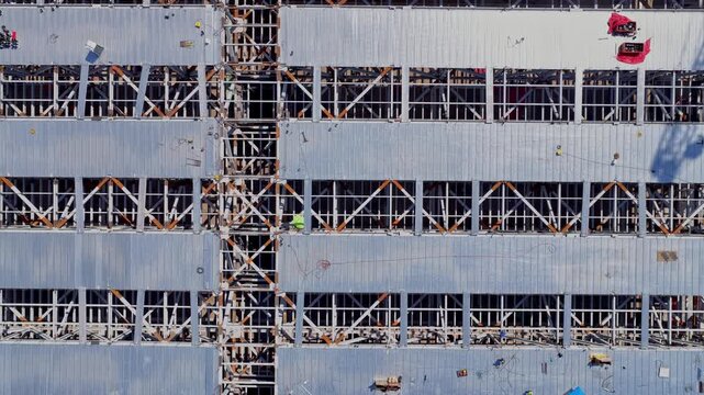 Texas Instruments LFAB2 semiconductor fab with multi-level steel framing, metal decking, vertical bracing, construction platforms and workers in Lehi, Utah, USA, top-down drone ascent