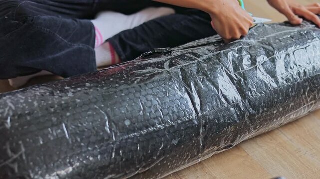 Close-up on hands carefully cutting open plastic bubble wrap packaging with scissors on floor