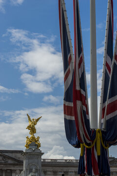 View of the golden Victoria Memorial statue with draped Union Jack flags against a blue sky in London, England, United Kingdom.