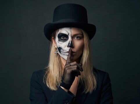 Woman with half skull face paint wearing top hat making silence gesture for halloween concept