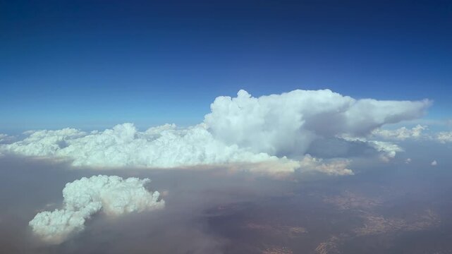 An aerial view of massive pyrocumulus storm clouds originated by wildfires in central Spain in summer 2026, with a view of the tops emerging though the smoke, under a blue sky.