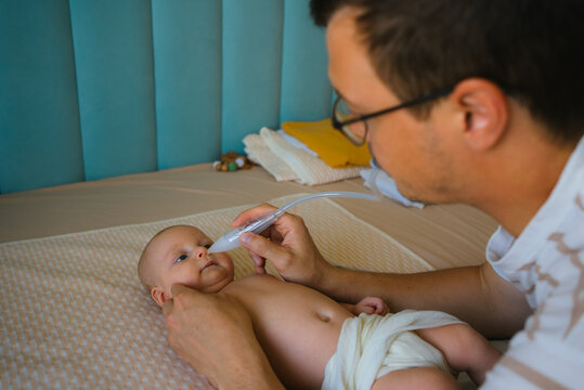 Father gently uses a nasal aspirator to clear his newborn's congested nose, providing hands on care and comfort during routine infant health and hygiene at home