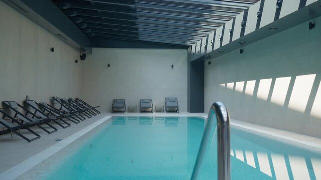 Boutique resort indoor swimming pool features clean turquoise water and sunbeds. This modern wellness center provides a serene atmosphere for luxury spa vacation and peaceful relaxation.