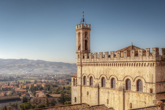 View of Palazzo dei Consoli with its medieval stone architecture and bell tower overlooking the valley in Umbria, Italy.