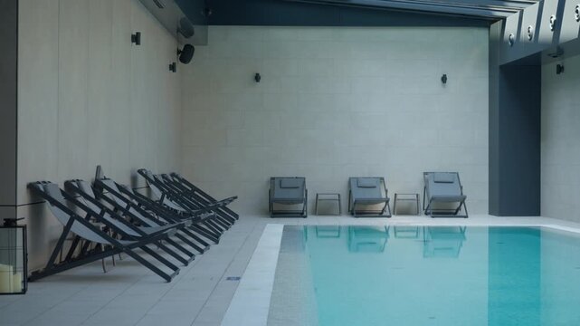 Modern spa wellness center features comfortable lounge chairs by an indoor pool. This quiet relaxation area provides a peaceful atmosphere for body recovery, serenity and healthy lifestyle.