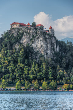 View of Bled Castle perched on a steep cliff above Lake Bled with lush green trees and a clear blue sky in Slovenia.
