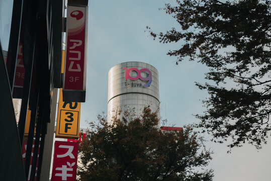 SHIBUYA, TOKYO JAPAN - NOVEMBER 16, 2023: 109 building stands prominently in background behind signage and trees in Shibuya, Tokyo