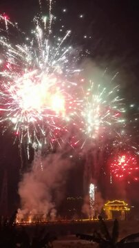 Vertical Video: Fireworks exploding over a small rural village on Chinese New Year's Eve with families celebrating together.