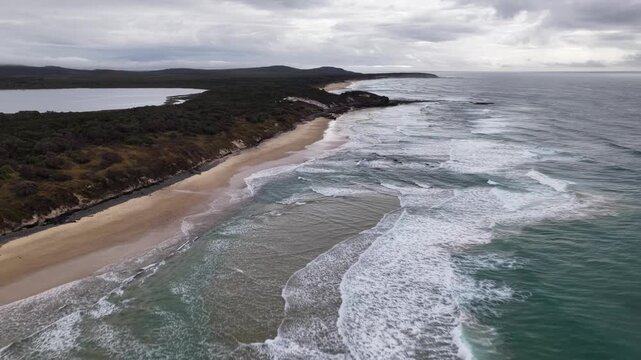 Aerial video flying over the rugged coastline at Lake Arragan, featuring sandy shoreline, rocky formations and waves rolling in from the Pacific Ocean