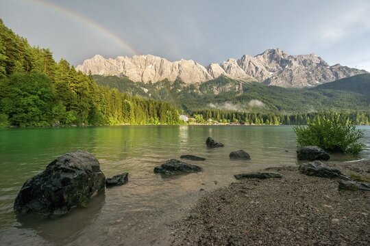 Rocks on the shore, Eibsee lake in front of Zugspitze massif with Zugspitze with rainbow, behind thunderclouds, Wetterstein range, near Grainau, Upper Bavaria, Bavaria, Germany