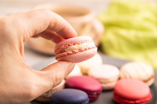 Macarons colourful cookies dessert with hand on brown concrete, close up, side view, selective focus