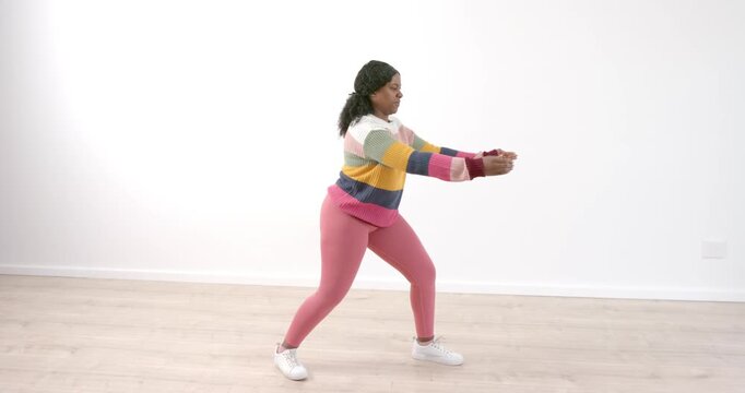 Woman practicing tai chi indoors, wearing colorful sweater and pink leggings