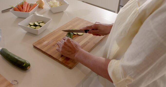 Slicing fresh zucchini on wooden board in modern kitchen, preparing healthy meal