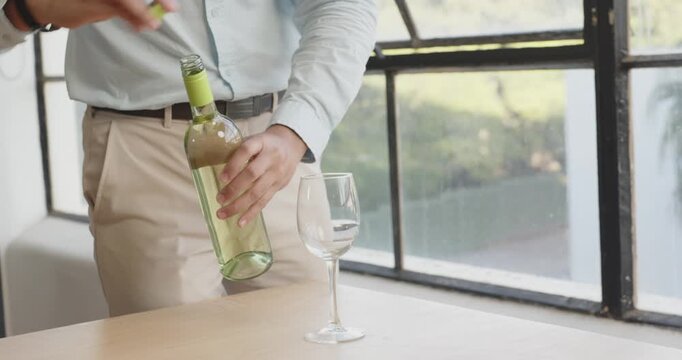 Man opening wine bottle and holding glass by large window in office