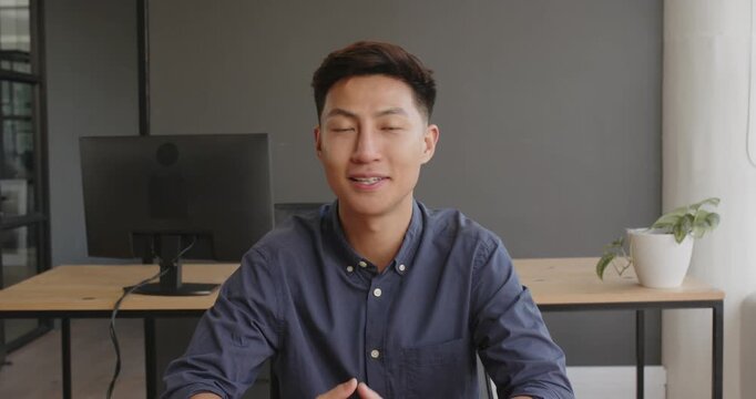 Asian man in office smiling with eyes closed, sitting at desk with computer