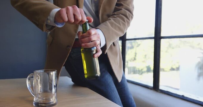 Businessman pouring beer into glass by large office window, enjoying break