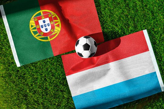 Portugal vs. Luxembourg football match. National flags on green grass with soccer ball in the middle. Football background for international match.
