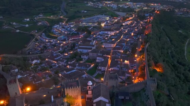 Aerial view of medieval walled town Obidos illuminated at night with ancient castle walls and pathways.