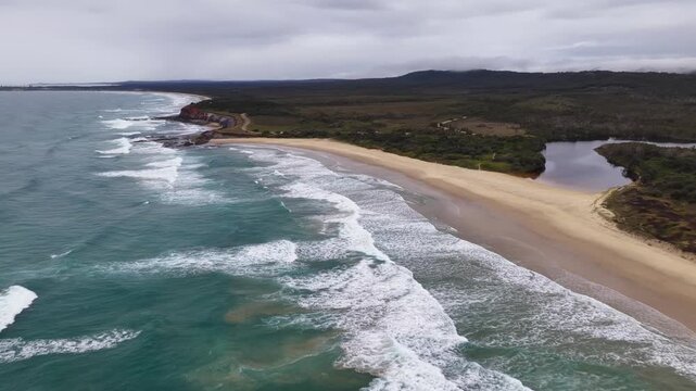 Aerial video flying over the rugged coastline at Lake Arragan, featuring sandy shoreline, rocky formations and waves rolling in from the Pacific Ocean