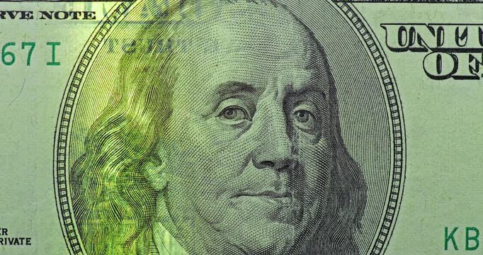 Benjamin Franklin portrait under green scan. 100 dollar bill with Benjamin Franklin portrait passes under moving green security scan. Zoomed close view highlights note security glow.