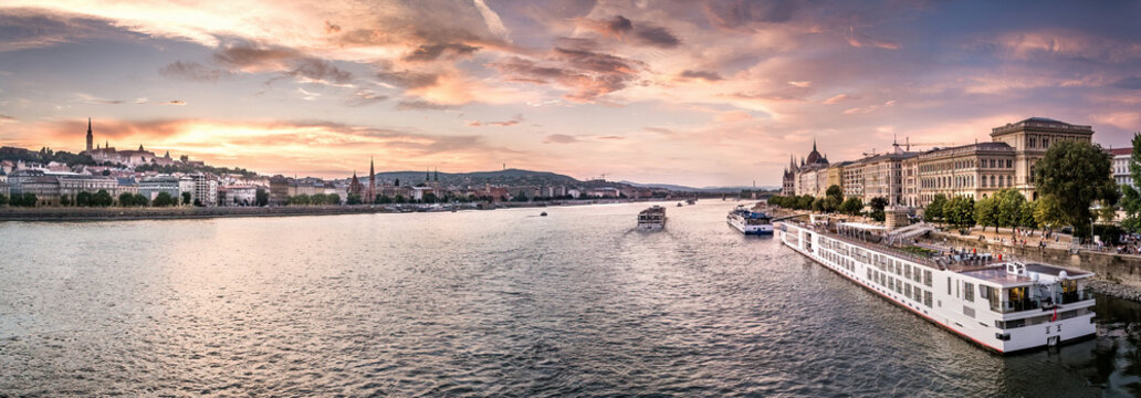 Panoramic view of Danube river with cruise ships and city skyline at colorful sunset in Budapest.