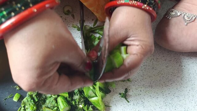Indian woman chopping fresh ridge gourd vegetable with traditional sickle knife close up