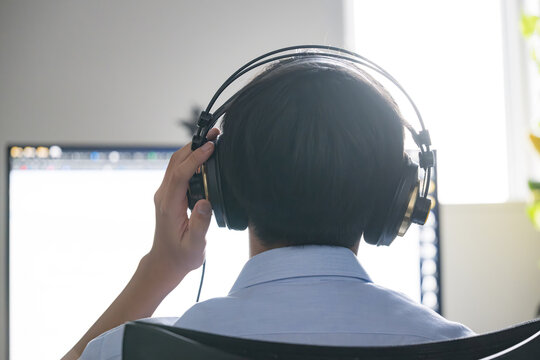 ヘッドホンをつけてパソコンで予備校のオンライン学習する高校生、自宅で授業やリスニング学習に取り組む、音楽を聴く、学生の後ろ姿