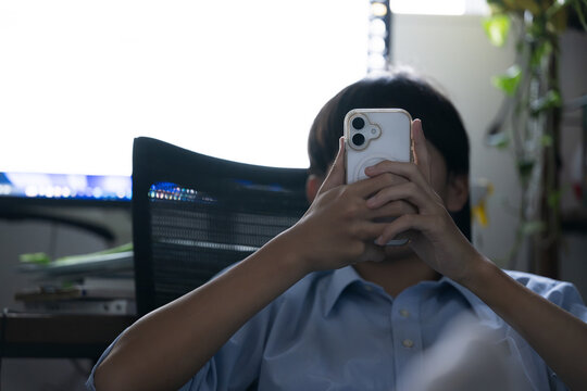 自宅で勉強に集中せずスマホを触る学生、学習中にスマートフォンに触れる学生、ドーパミン中毒注意　顔無しのイメージ