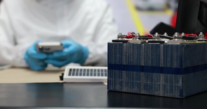 Close-up of a lithium battery pack on a workbench with a technician in protective gloves inspecting a device in a laboratory.