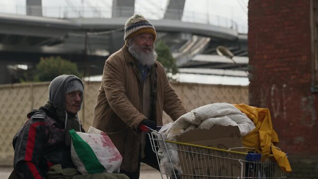 Senior Caucasian man pushing shopping cart beside young adult Caucasian man with disability in wheelchair. Useful for social welfare campaigns and poverty awareness documentaries