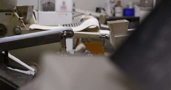 Industrial food production line with an automated machine processing fresh raw dough on a conveyor belt, preparing ingredients for baking inside a professional factory kitchen