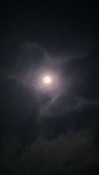 Full moon glows brightly behind dark clouds in the night sky.