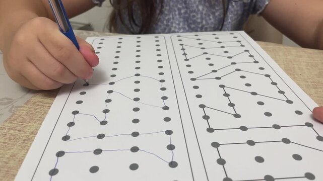 Focused little girl connecting dots with pen on logic worksheet during educational home assignment at table. High quality 4k footage