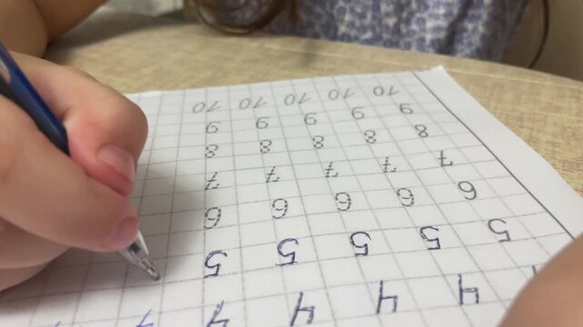 Extreme close up of child hand carefully tracing numbers with pen on practice copybook paper sheet at desk. High quality 4k footage