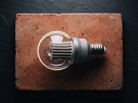 Modern energy-efficient LED light bulb lying on an aged red clay brick against a dark textured slate background