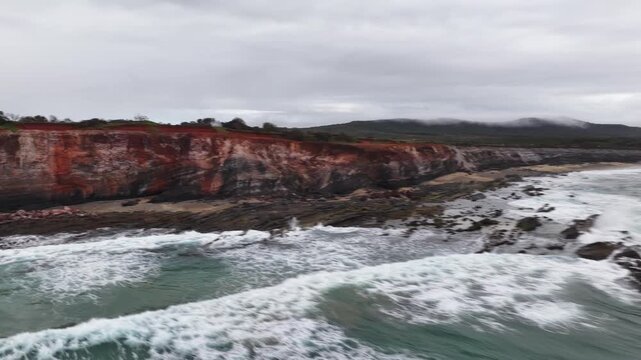 Aerial video flying over the rugged coastline at Lake Arragan, featuring sandy shoreline, rocky formations and waves rolling in from the Pacific Ocean