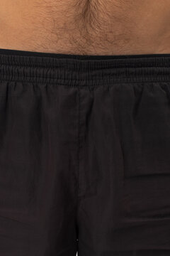 Close-up macro detail of a man wearing dark brown elastic waistband shorts. Showing hairy abdomen skin and waistband stitching. Ideal for clothing detail, textiles, and mens fashion stock.