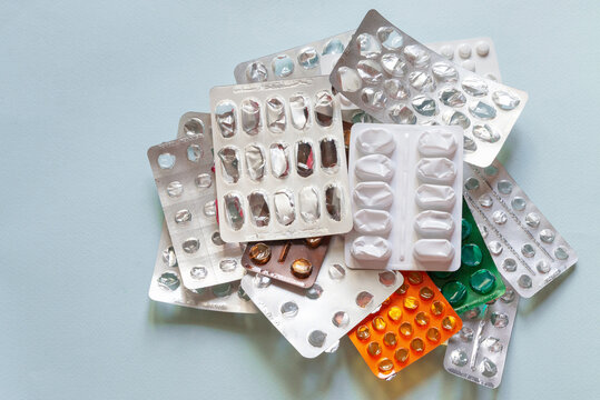 Empty medicine blister packs piled in a heap on blue background, used pharmaceutical packaging illustrating medication consumption, medical waste, recycling, disposal, pharmacy services and environmen