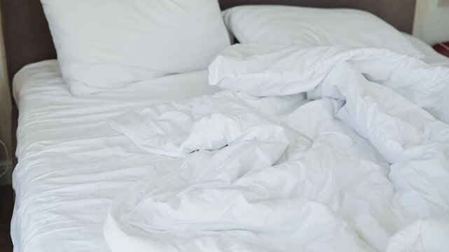 A bed is shown with white wrinkled sheets and two white pillows. The setting has a simple indoor environment, suggesting it might be a guest room