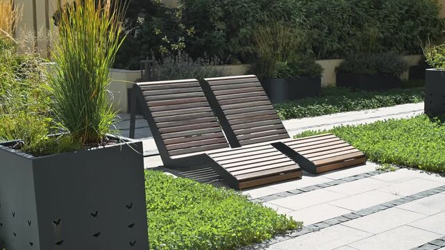 Lounge chairs are positioned in a garden environment surrounded by greenery and modern planters. The arrangement showcases a contemporary outdoor design with clean lines and natural elements