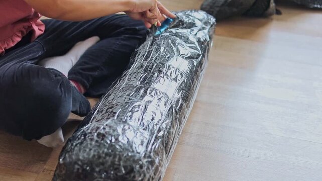 Close-up on hands slicing open plastic bubble wrap packaging with knife while sitting at home